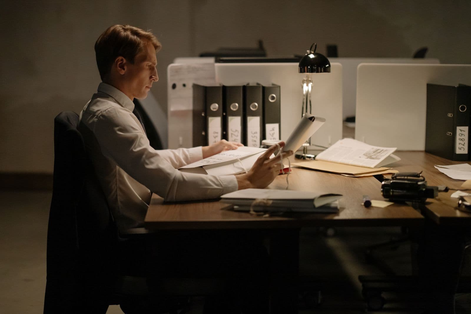 An office worker in formal attire reading a document closely at a desk