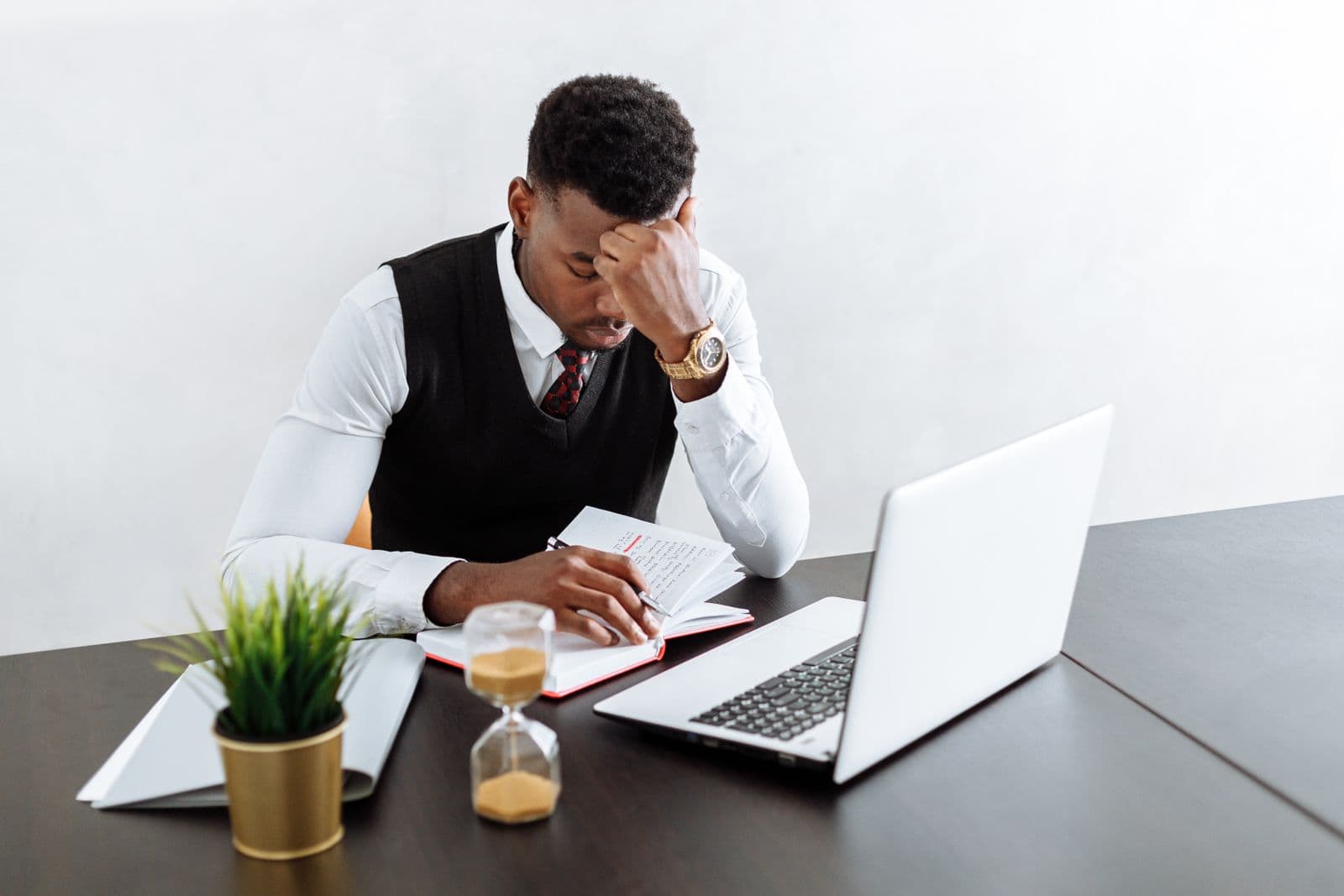A businessman working at a laptop beside an hourglass running out of sand.